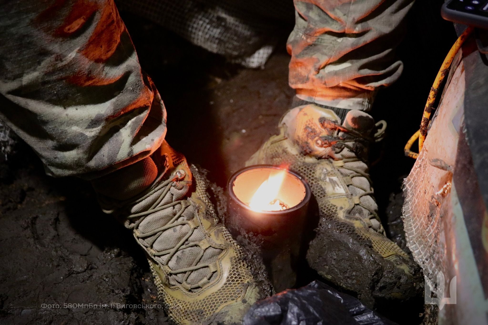 Захисник України гріє ноги окопною свічкою.