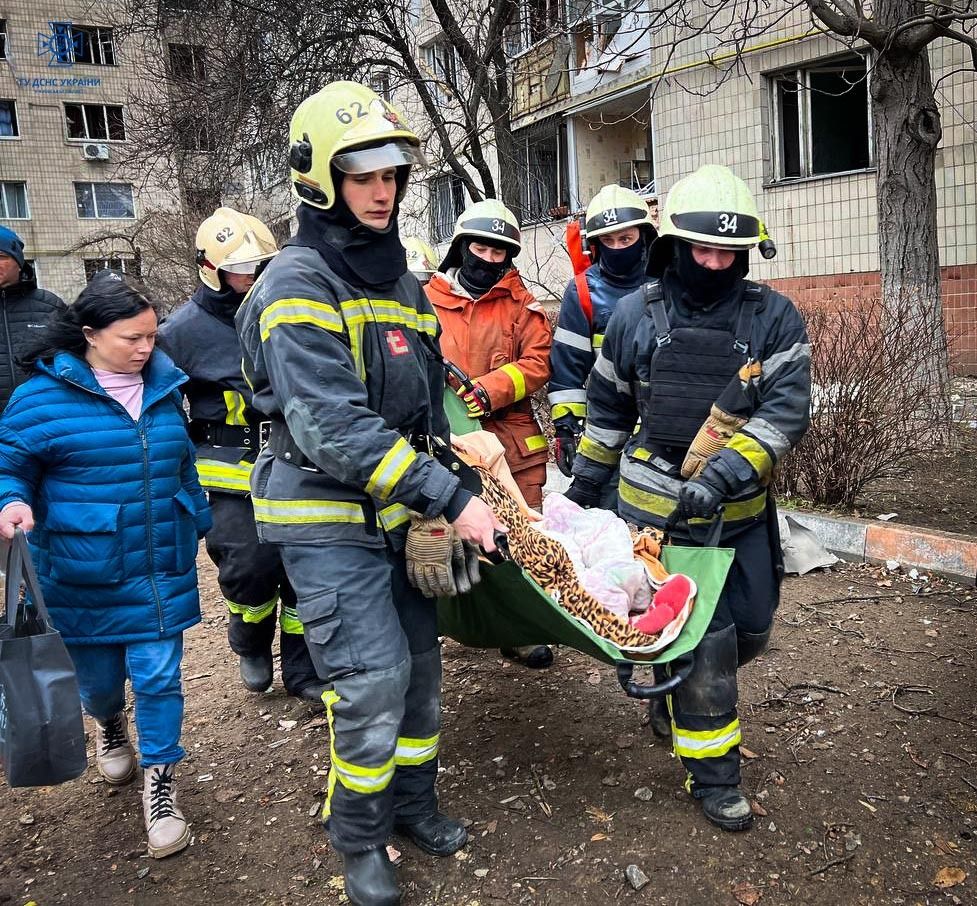 Рятувальники несуть до «швидкої» літню жінку, якій стало зле після ворожої атаки у Вишневому на Київщині 2 січня.
